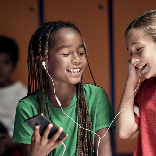 Two girls sharing headphones listening and smiling together