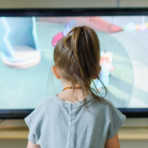 Preschool age girl sitting in front of a television watching the screen