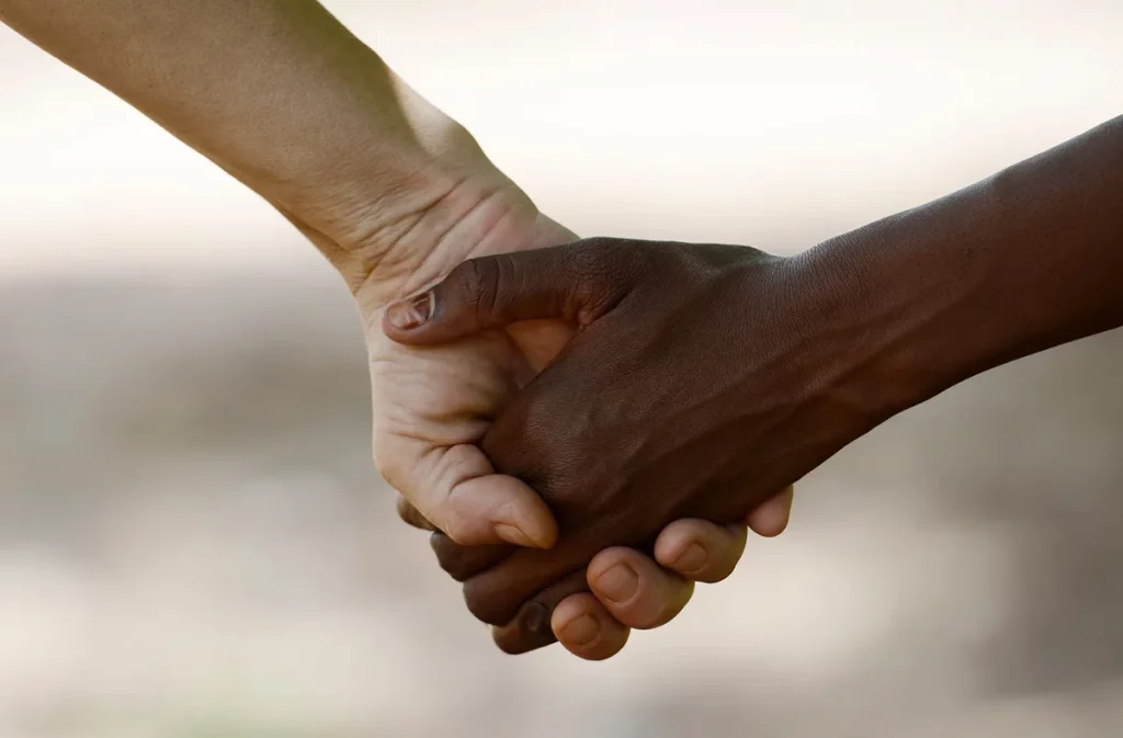 Two hands of different colors holding each other
